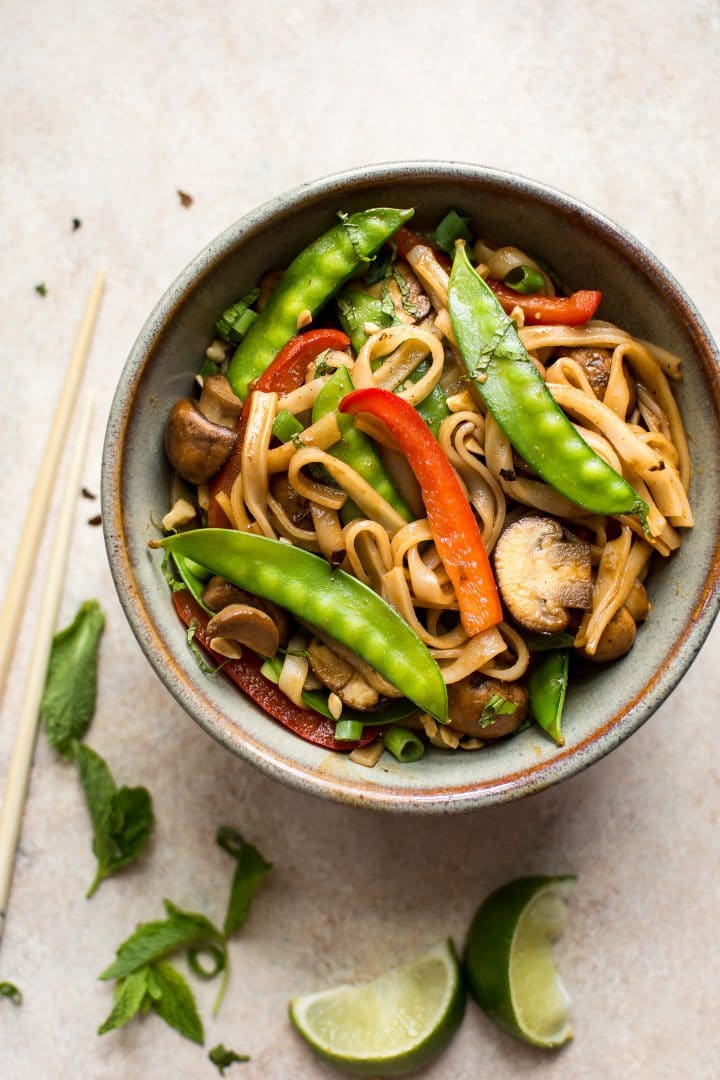 vegan rice noodle stir fry with vegetables in a bowl beside lime slices and chopsticks