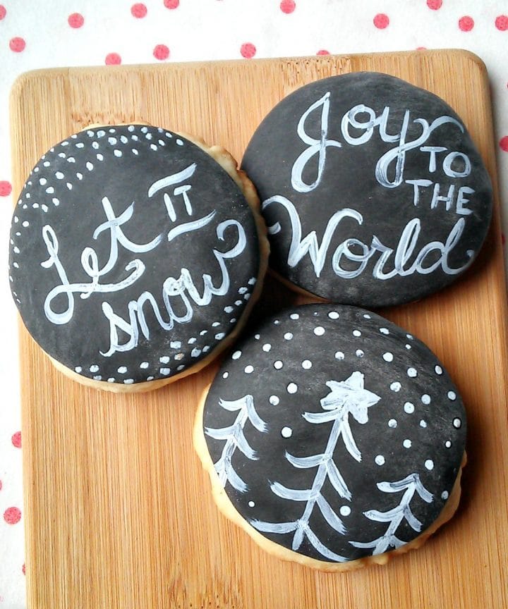 sugar cookies on a wooden board that look like chalkboard with messages that read let it snow and joy to the world