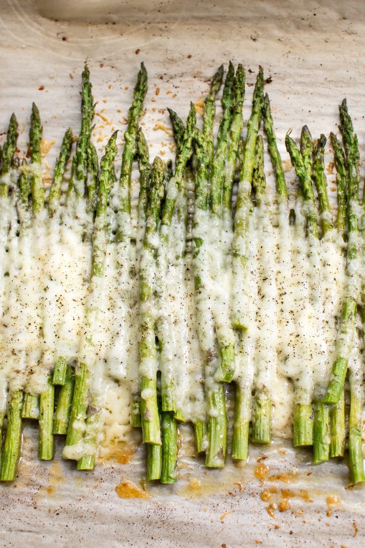 several spears of easy cheesy baked asparagus on parchment paper