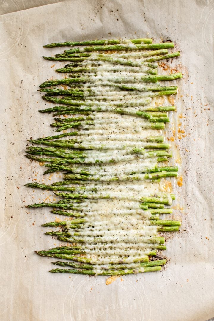 several spears of cheesy garlic roasted asparagus with melted parmesan and mozzarella on a baking sheet