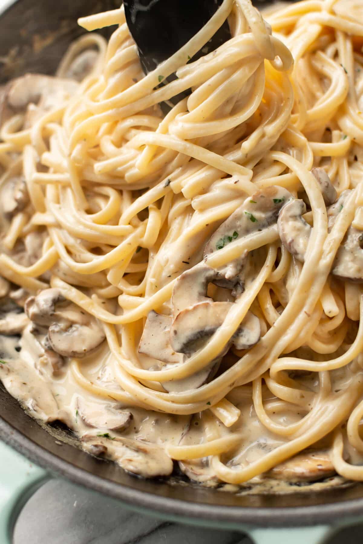 closeup of a skillet with creamy mushroom pasta and kitchen tongs