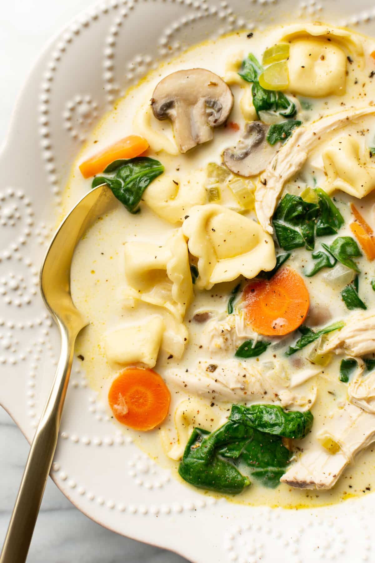 a bowl of creamy spinach chicken tortellini soup with a spoon