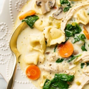 a bowl of creamy spinach chicken tortellini soup with a spoon