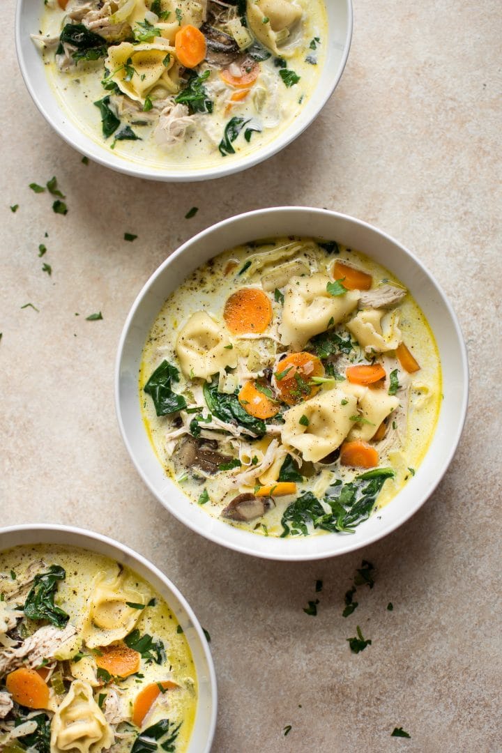three white bowls with creamy chicken spinach tortellini soup