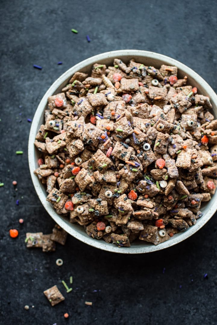 Halloween muddy buddies with Halloween themed sprinkles in a bowl on a dark surface