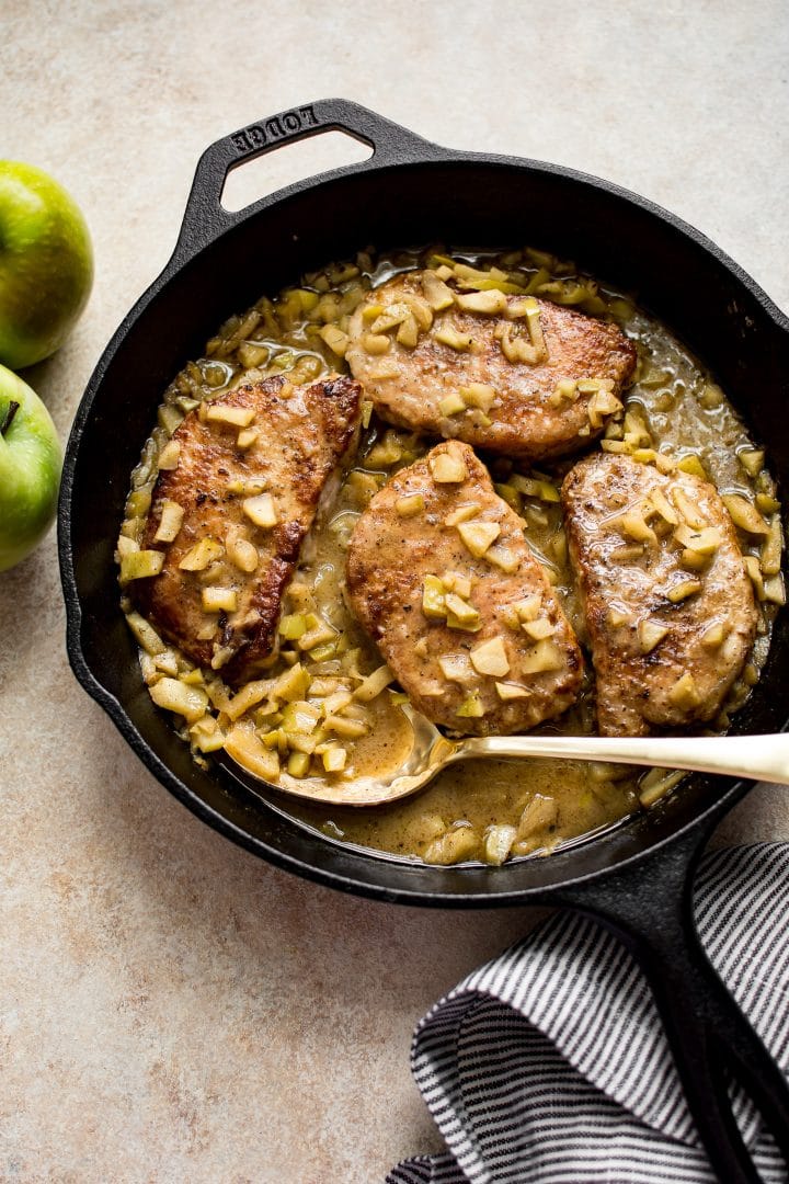 pork chops with chopped apples in a butter sauce in a skillet with a serving spoon