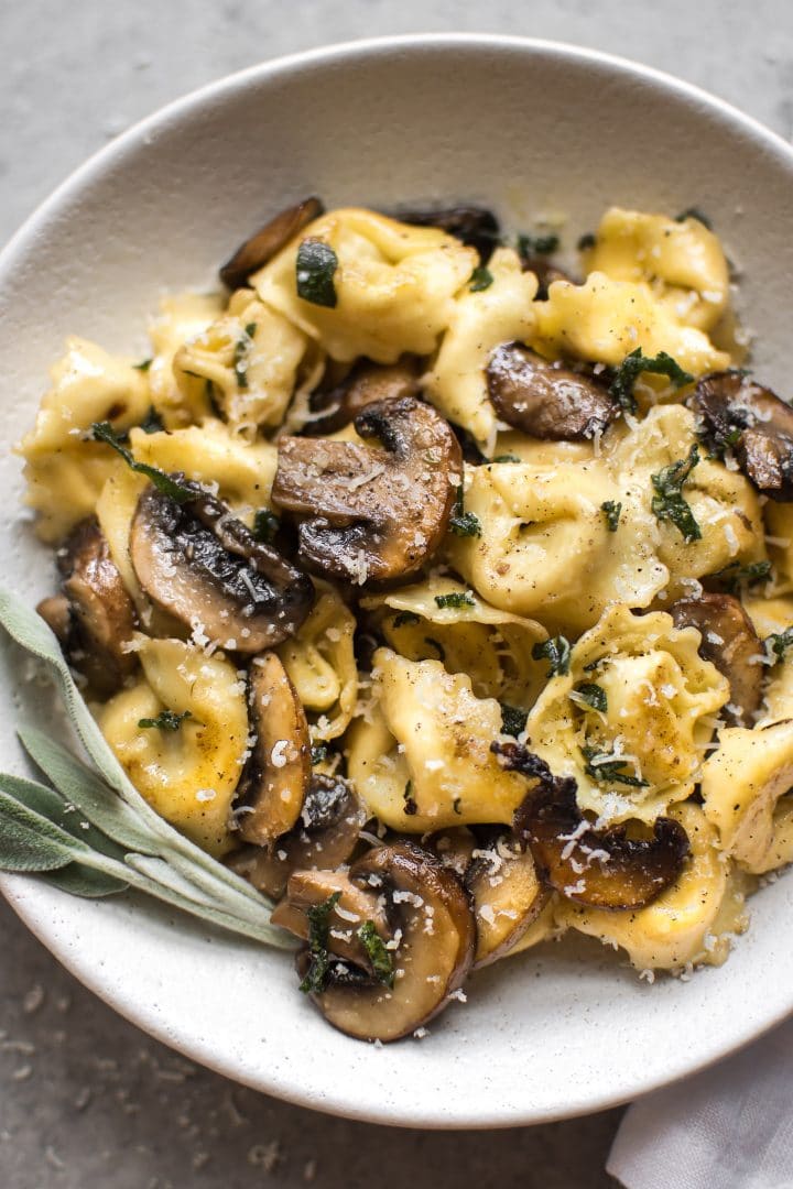 close-up of tortellini with a mushroom, crispy sage, and butter sauce in a white bowl