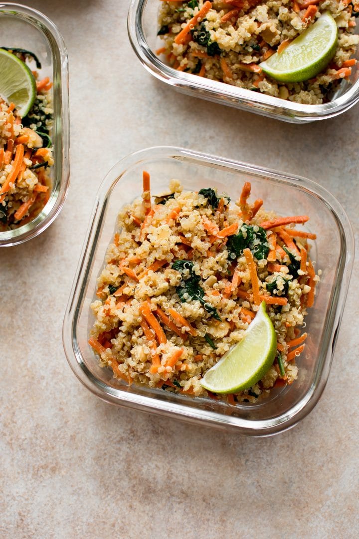 close-up of glass container with vegan meal prep bowls recipe with spinach, carrots, quinoa, lime slice, and a light dressing