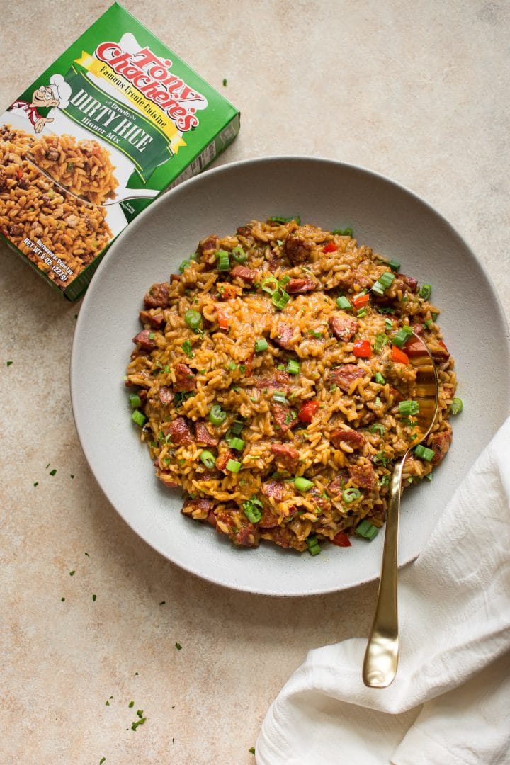 dirty rice dressing with andouille sausage and red peppers in a bowl next to box of Tony Chachere's dirty rice dinner mix