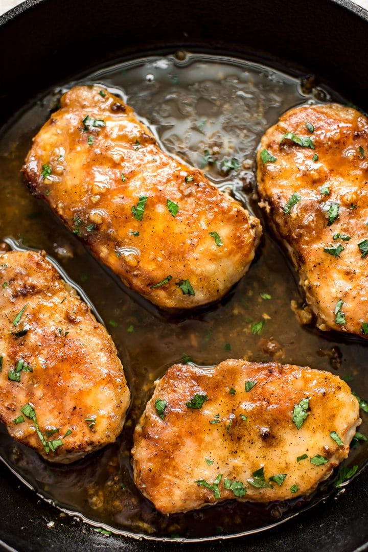 close-up of four pork chops with a soy sauce and honey sauce in a skillet