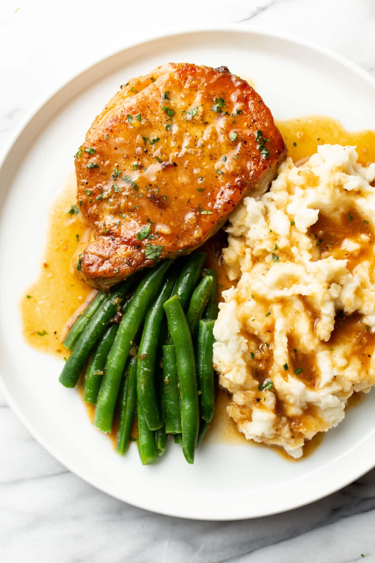 a plate with a pork chop, green beans, mashed potatoes, and honey garlic sauce