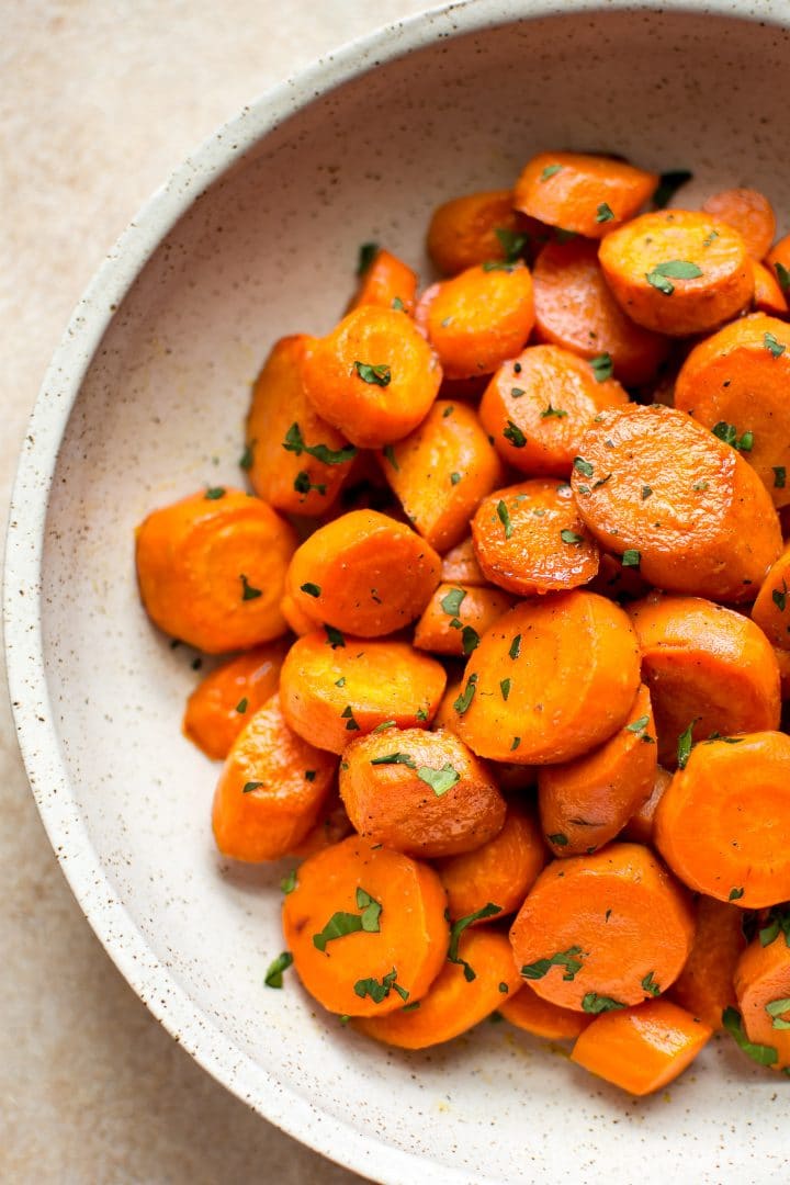 close-up of vegan maple roasted carrots with chopped parsley garnish in a beige bowl
