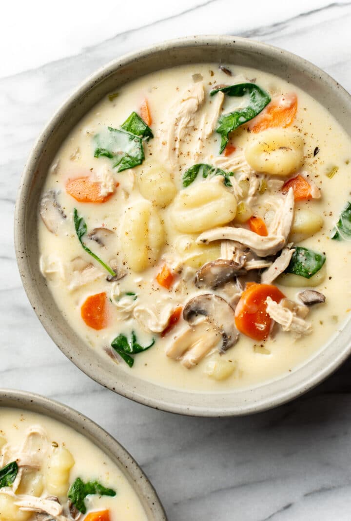 two bowls of easy chicken gnocchi soup on a marble surface