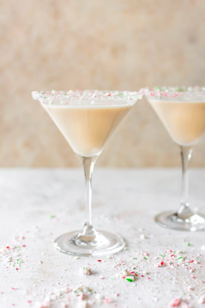 two martini glasses of creamy festive holiday cocktail and red and green crushed candy cane rims