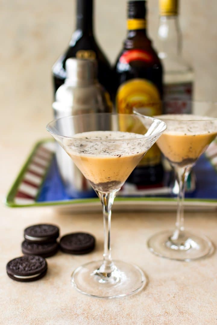 two martini glasses with festive christmas cookie cocktail next to four oreos