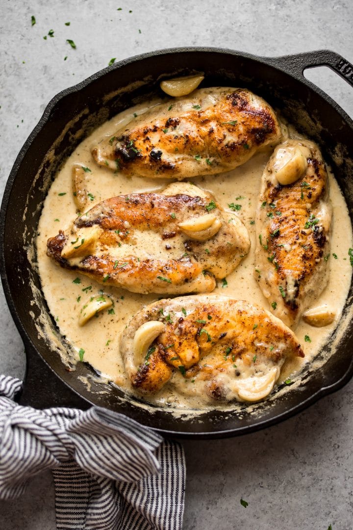 cast iron skillet with chicken breasts and a creamy garlic sauce with whole cloves of garlic