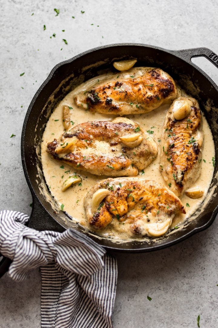 creamy garlic chicken in a cast iron skillet with whole garlic cloves and plenty of garlic cream sauce