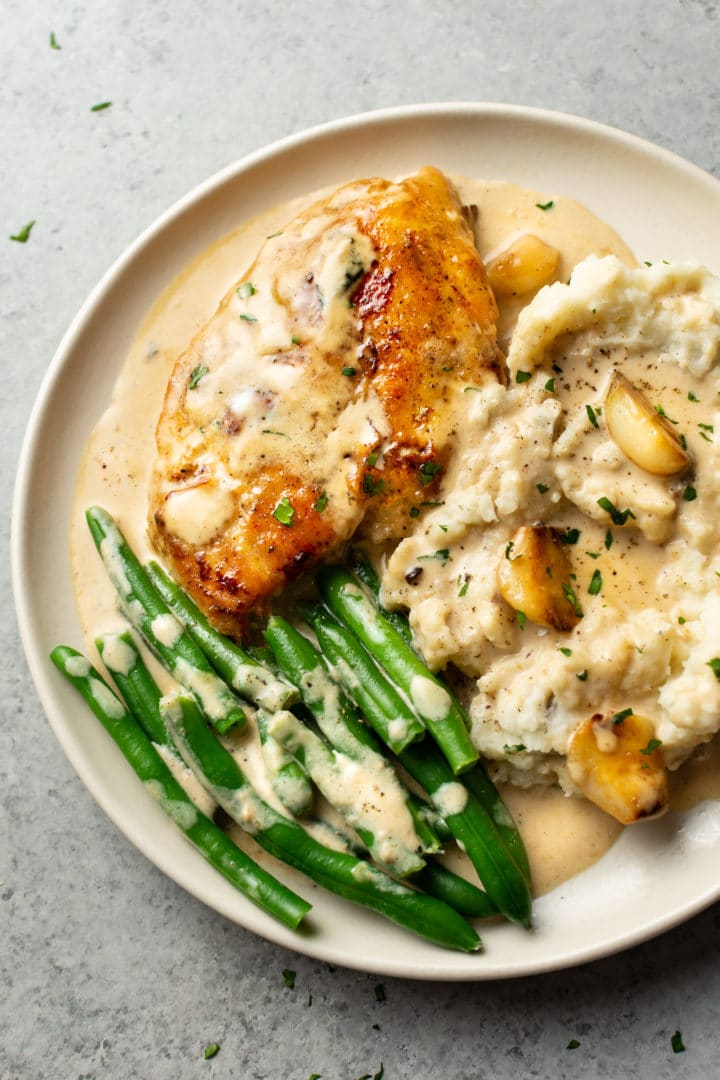 creamy garlic chicken on a plate with mashed potatoes and green beans