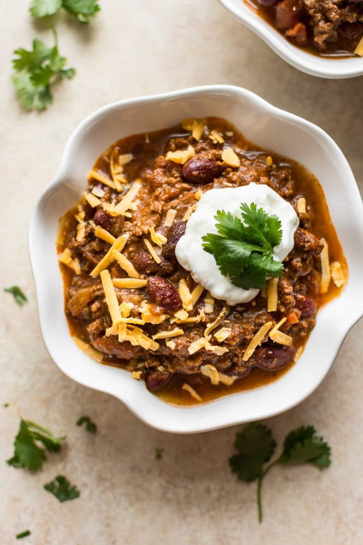 white bowl with electric pressure cooker beef chili topped with sour cream, cheese, and cilantro