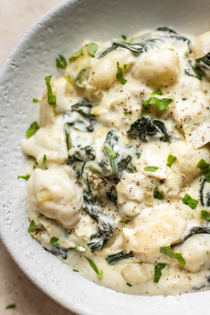 close-up of creamy spinach and artichoke dip gnocchi in a bowl