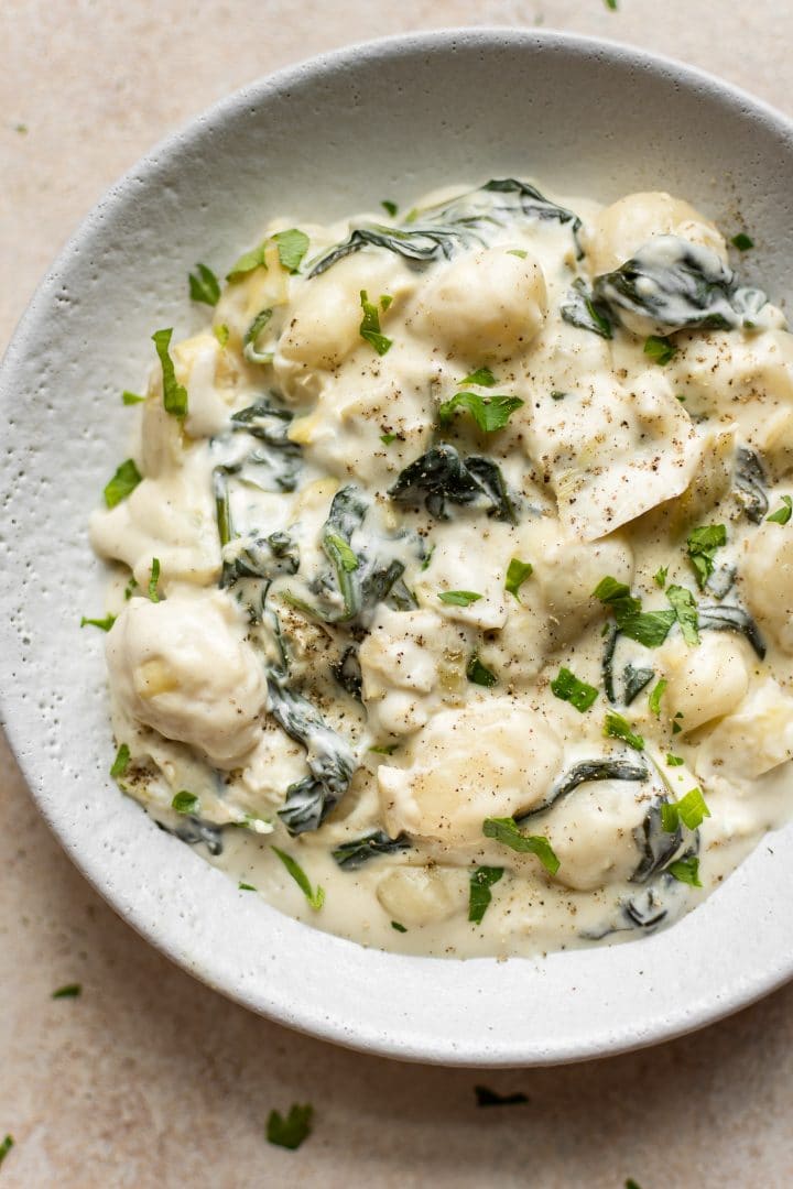 close-up of creamy spinach and artichoke gnocchi in a white bowl