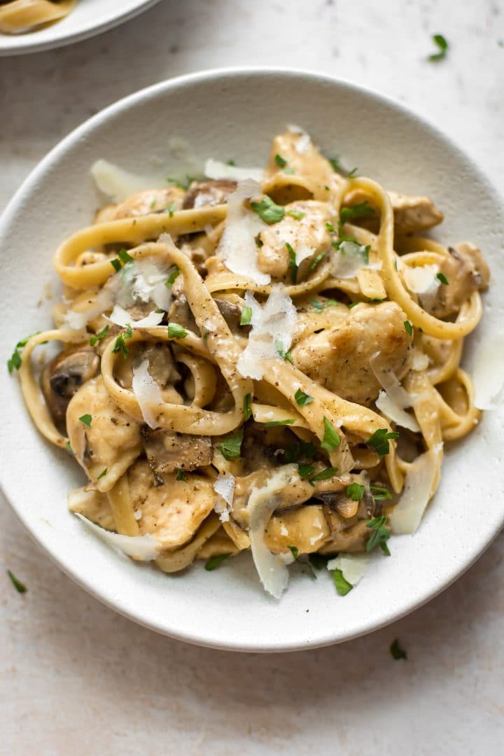 close-up of tender chicken marsala tossed with mushrooms, pasta, a creamy sauce, and grated parmesan in a bowl