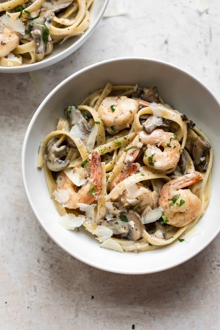 white bowl with shrimp and mushroom pasta topped with shaved parmesan