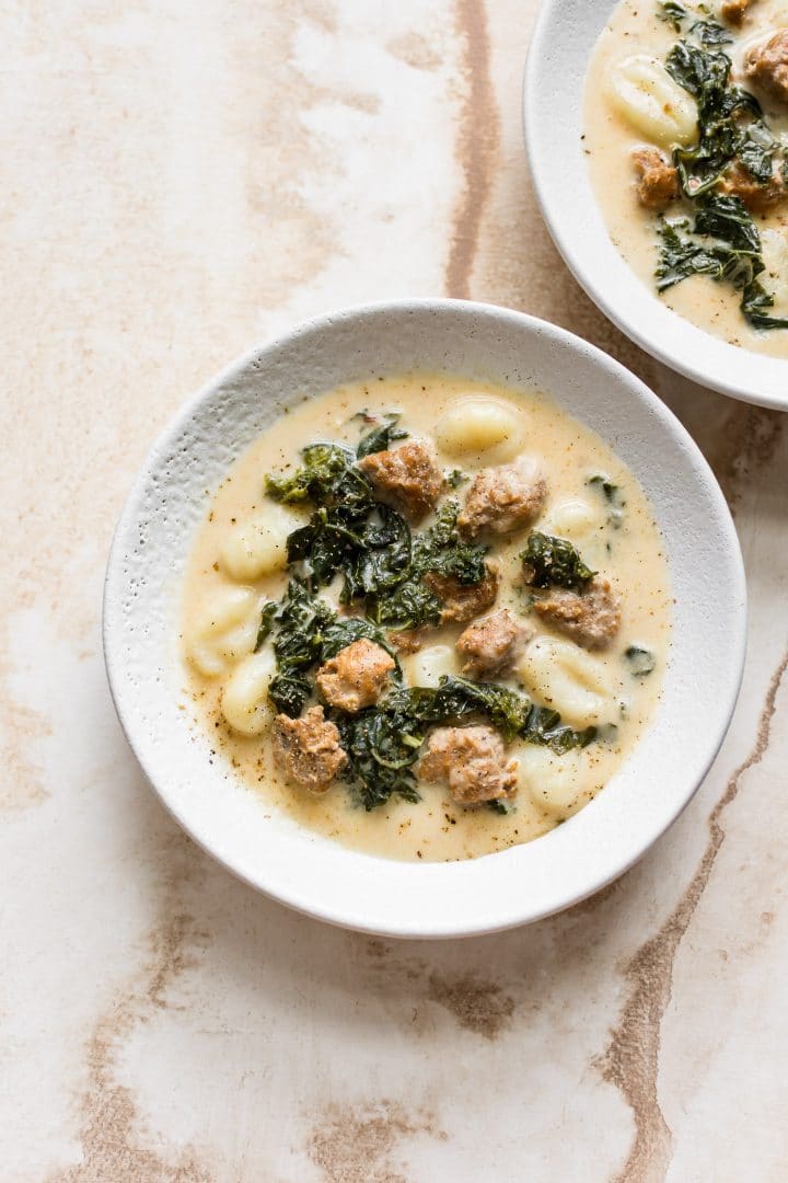 two white bowls of creamy sausage soup with gnocchi and kale
