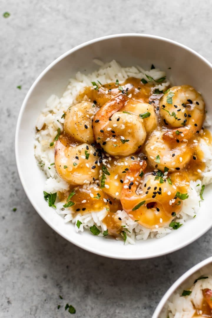 white bowl with sesame garlic shrimp over rice topped with sesame seeds