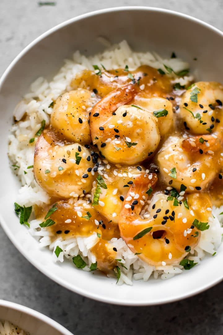 close-up of white bowl with honey ginger shrimp with garlic, sesame seeds, ginger, sesame oil, and soy sauce served over rice