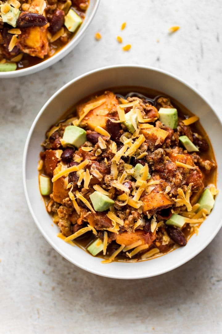 white bowl with healthy sweet potato ground turkey chili topped with avocado