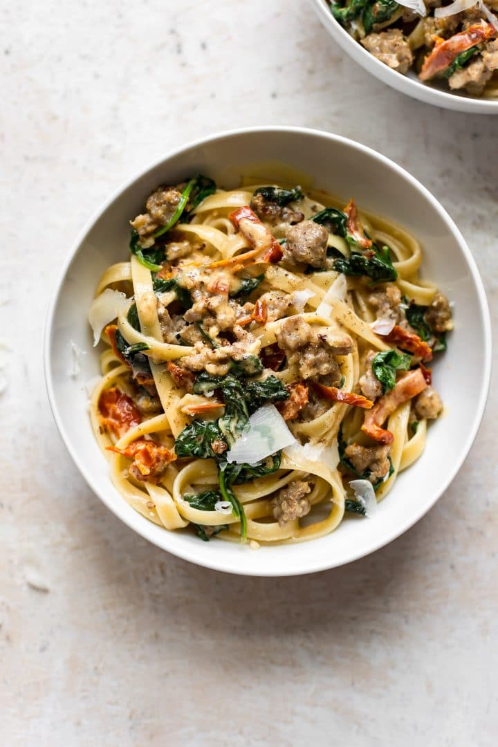 white bowl with easy Tuscan sausage pasta with a creamy sauce and grated parmesan