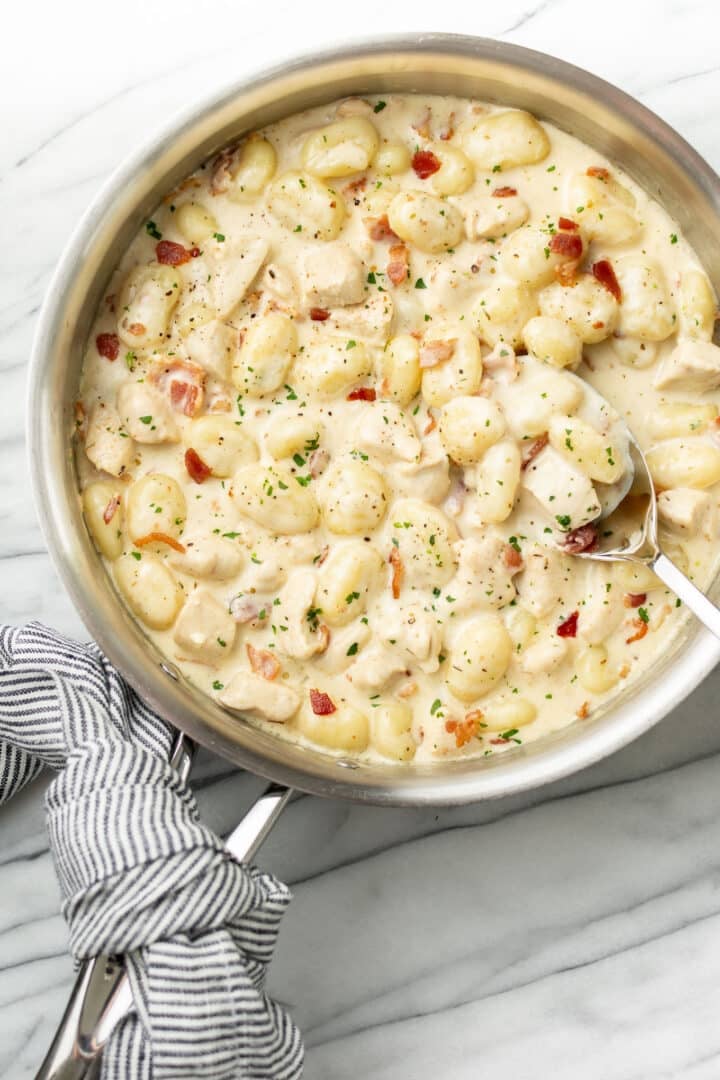 a skillet with chicken gnocchi with bacon and a serving spoon