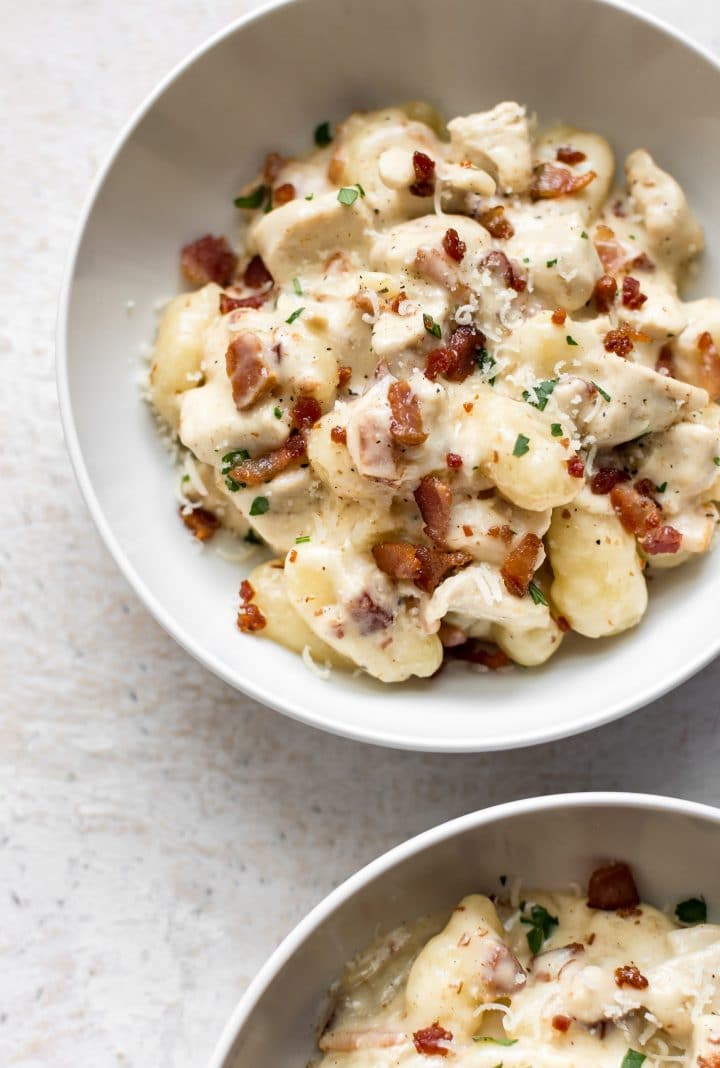 creamy chicken gnocchi with bacon in two white bowls with grated parmesan