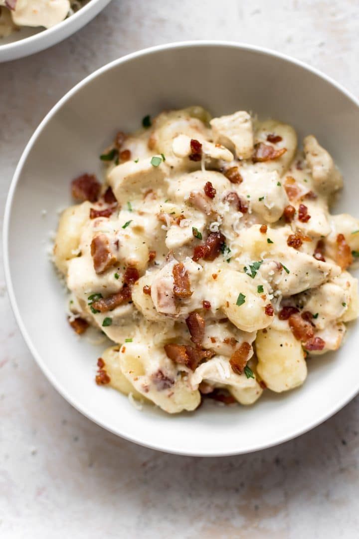 close-up of a white bowl with chicken, gnocchi, bacon, and a cream sauce