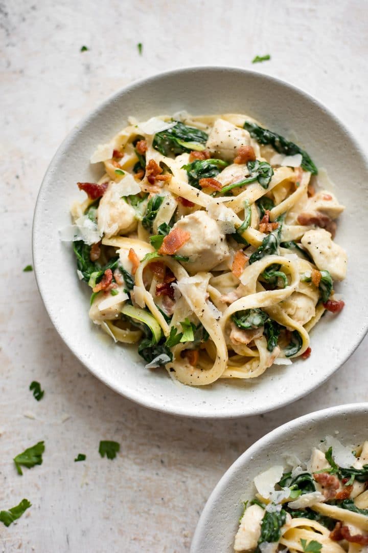 two white bowls of pasta with bacon and spinach and tender chicken