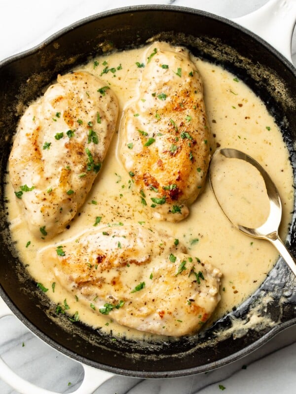 creamy white wine chicken in a skillet with a serving spoon