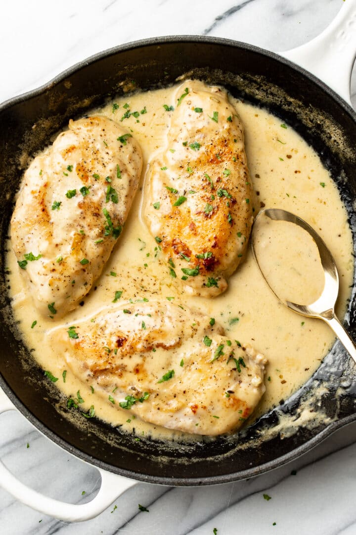 creamy white wine chicken in a skillet with a serving spoon