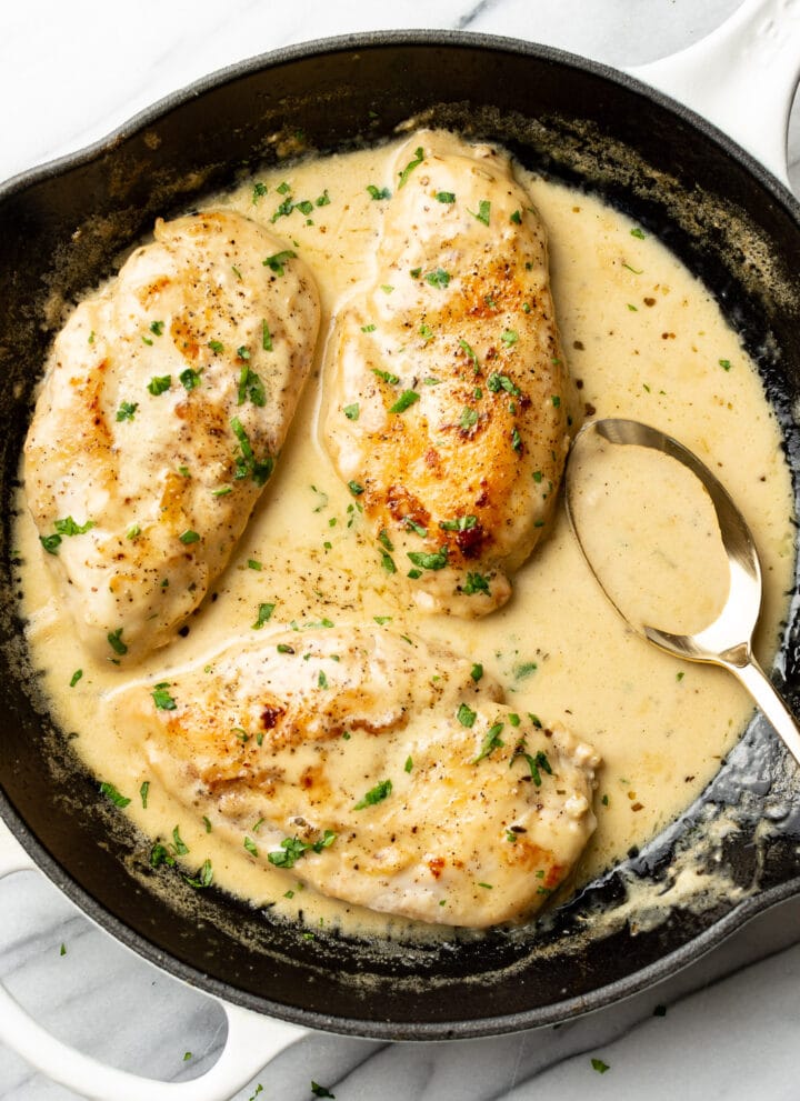 creamy white wine chicken in a skillet with a serving spoon