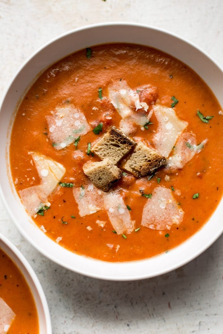 close-up of a white bowl with easy tomato soup topped with three croutons and shaved parmesan cheese