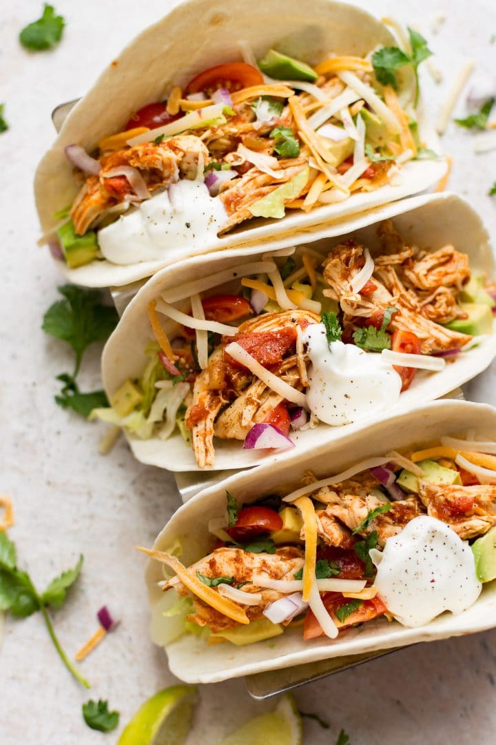three Instant Pot chicken tacos with sour cream beside lime wedges