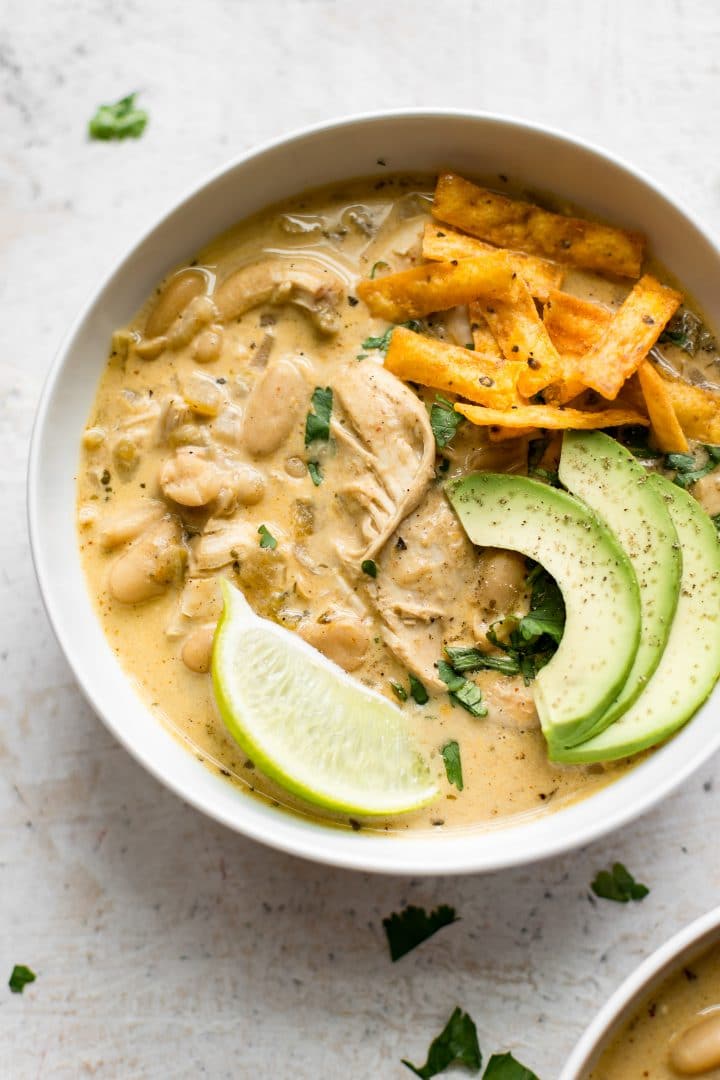 creamy white chicken chili in a white bowl with avocado and lime