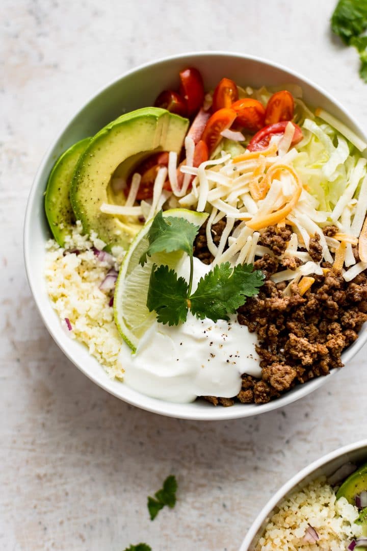 close-up of easy beef taco bowl with lime, avocado, shredded cheese, cilantro, sour cream, lettuce