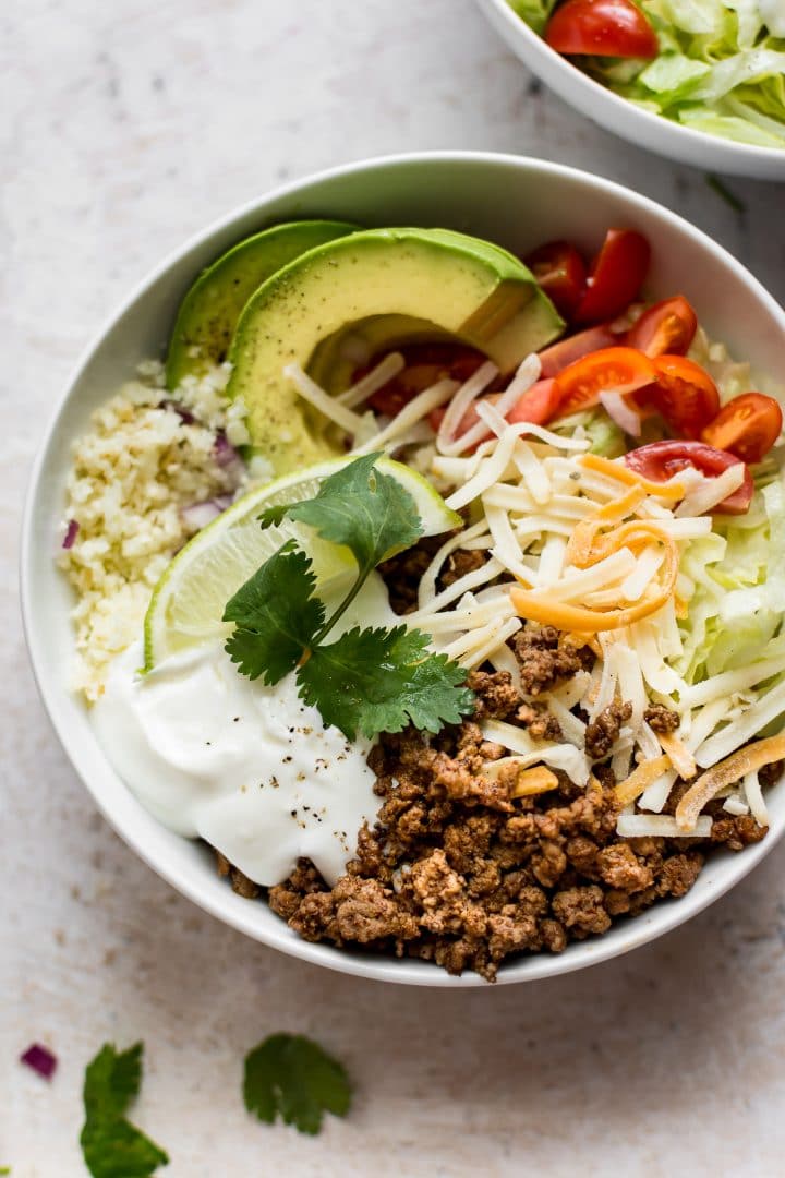 keto beef taco bowl with cauliflower rice topped with little tomatoes, sour cream, cilantro, and avocado slices