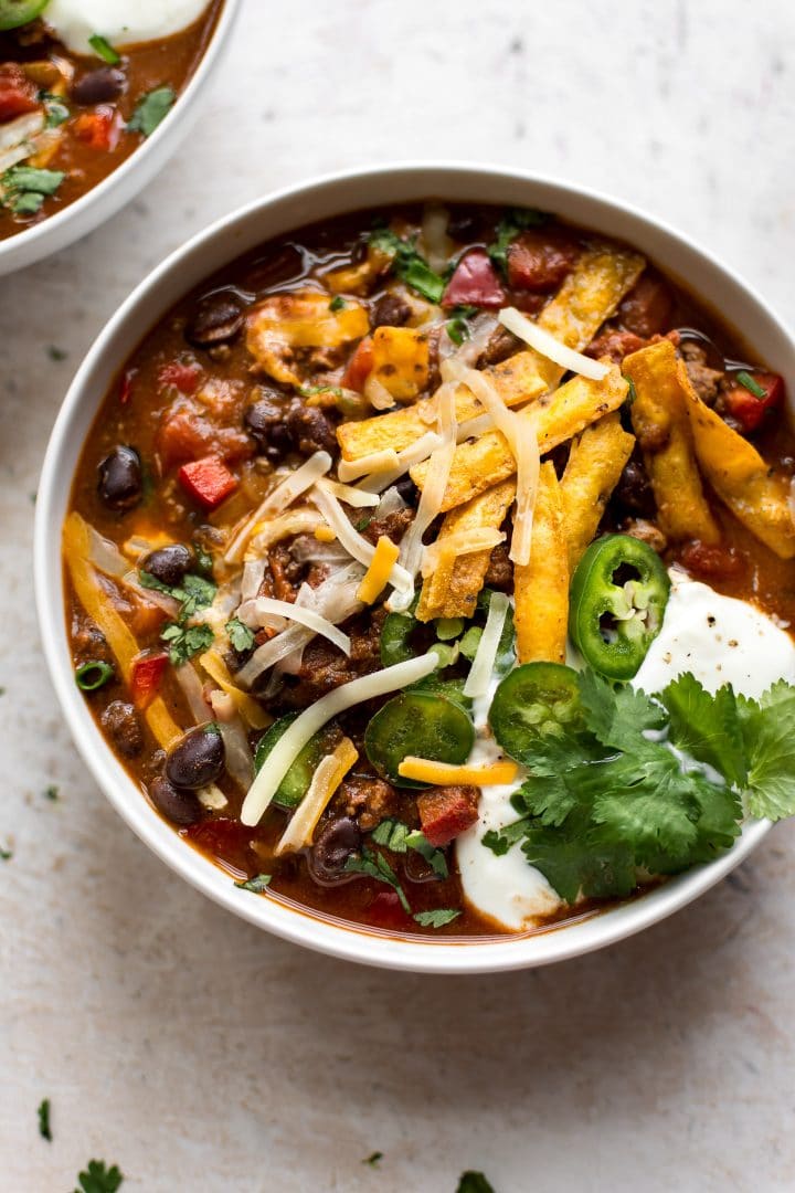 bowl of easy black bean chili with sliced jalapeno, sour cream, cilantro, and tortilla chips