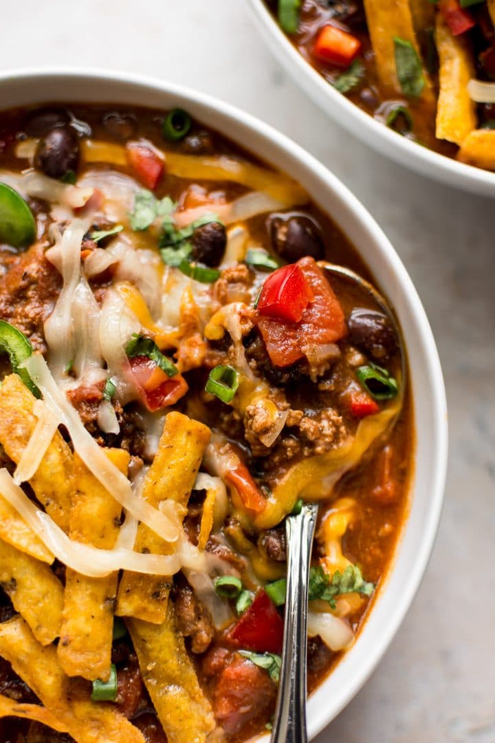 close-up of the best black bean chili in a white bowl with a spoon and tortilla chips