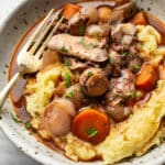 coq au vin in a bowl over mashed potatoes with a fork