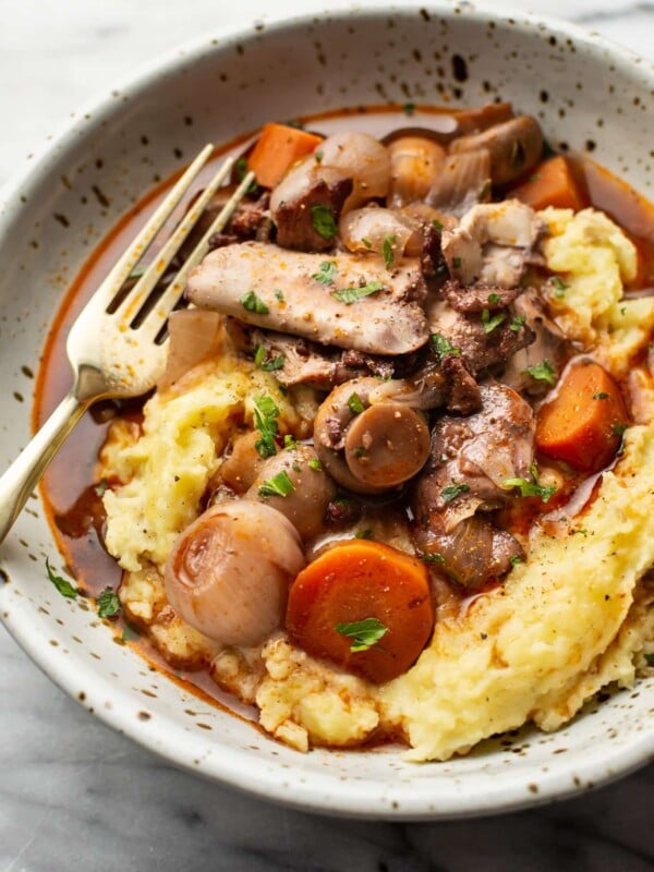 coq au vin in a bowl over mashed potatoes with a fork