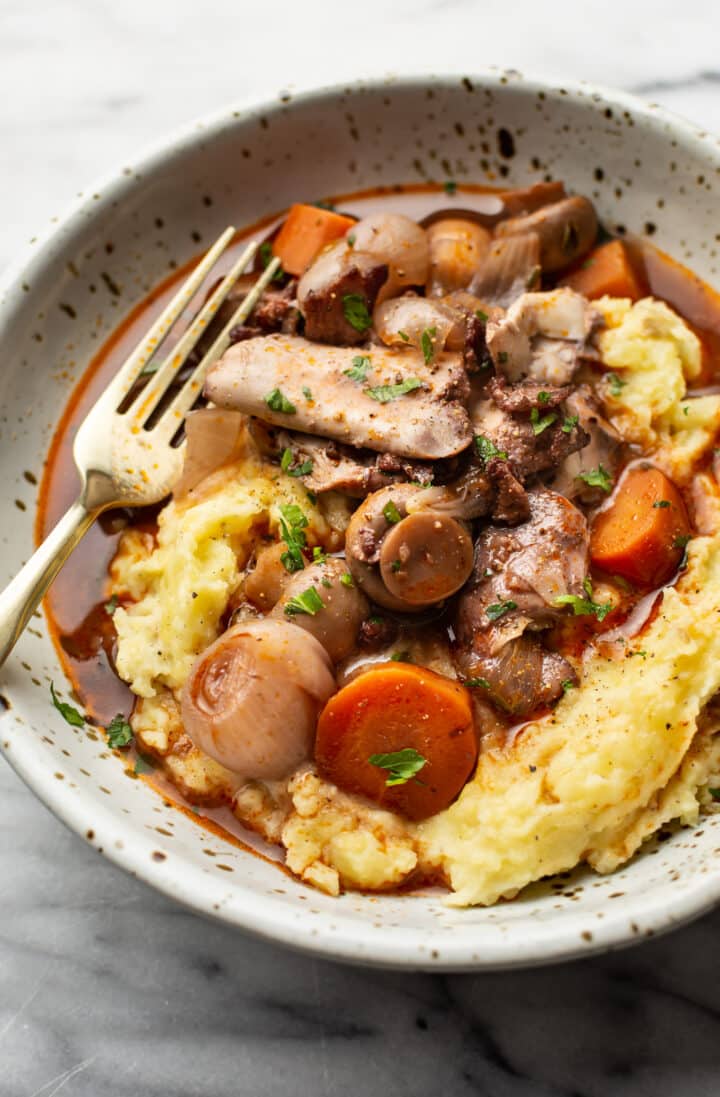coq au vin in a bowl over mashed potatoes with a fork