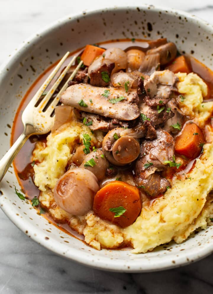 coq au vin in a bowl over mashed potatoes with a fork